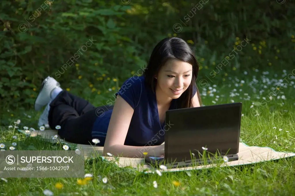 A young woman laying on a mat while using a wireless laptop in a park