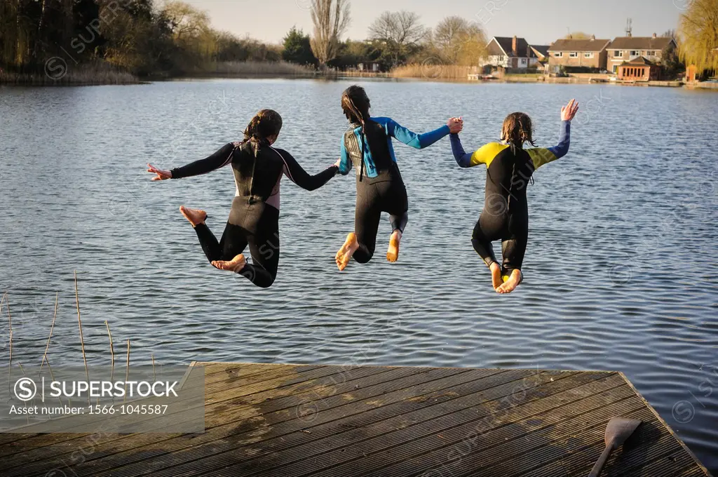 Three girls jumping into a lake while holding hands, England, UK