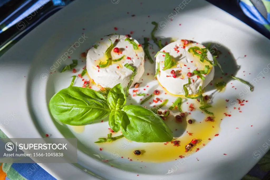 Small round goats cheeses with basil and red pepper on a white plate