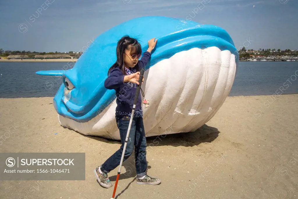 A blind Asian-American girl feels the outline of a waterside model whale while guiding herself with a white cane at an Easter picnic given by the Blin...