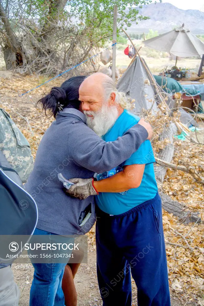 A Hispanic charity representative hugs a homeless military veteran at an outdoor encampment in the desert town of Victorville, CA  Note makeshift hous...