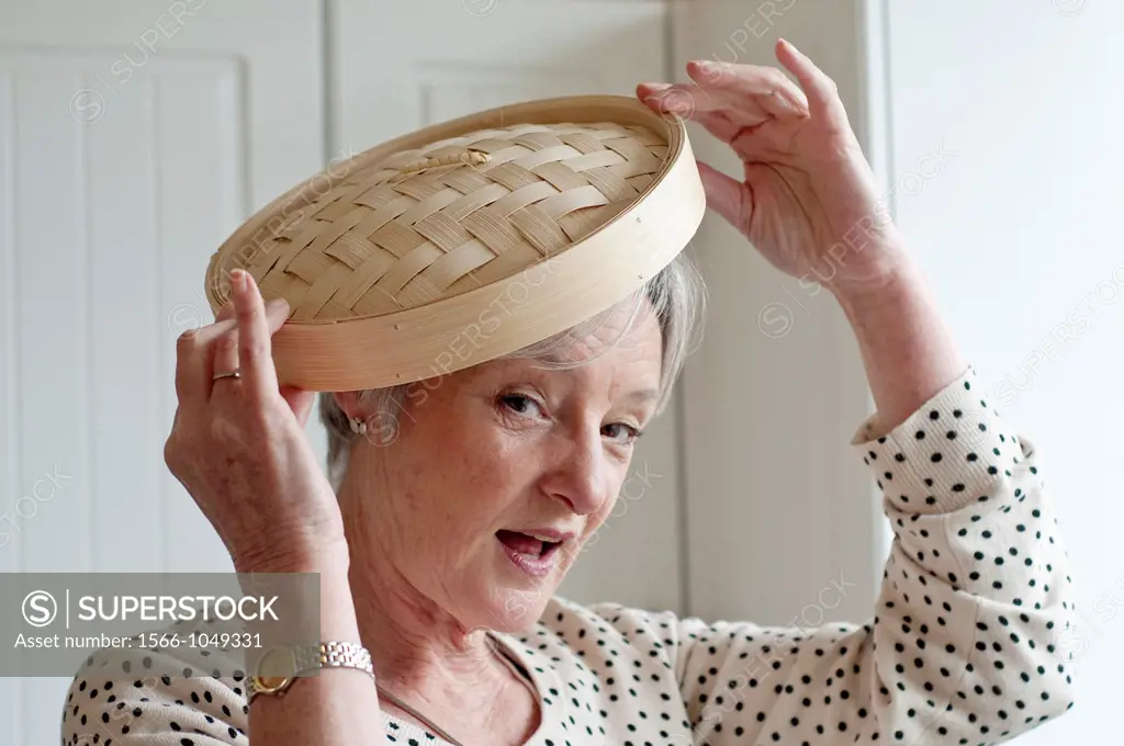 Middle aged woman playing with bamboo lid in kitchen