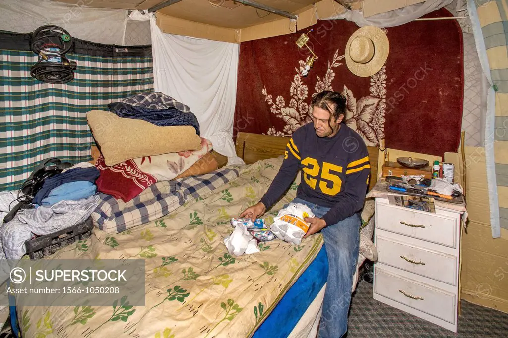 On the bed of his makeshift shelter among homeless residents of a primitive outdoor encampment in the desert town of Victorville, CA, an indigent mili...