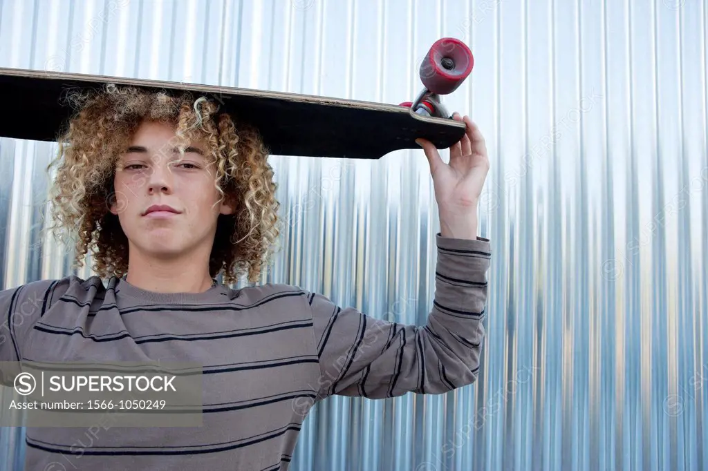 Teenage boy holding a longboard on his head