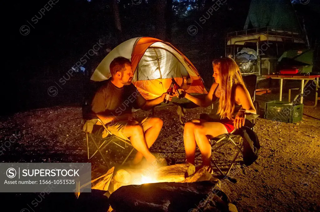 Couple by campsite fire with tents Sebago Lake Maine USA