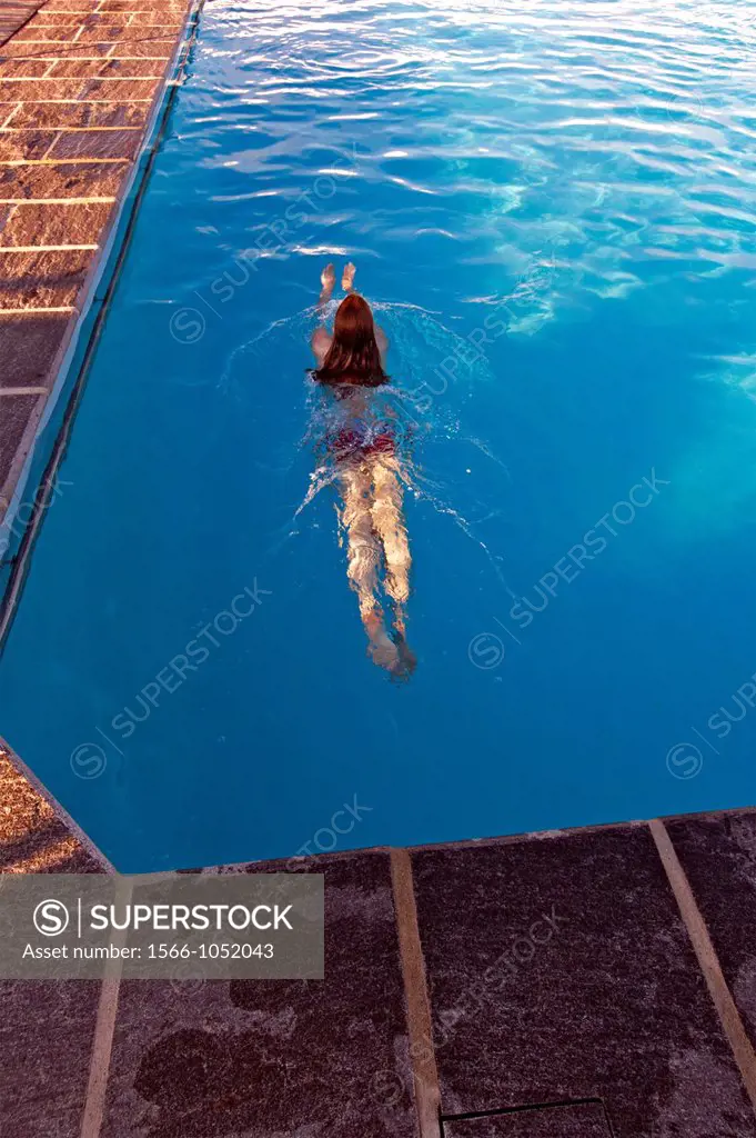 single young woman with long wet hair swimming in swimming pool at sunset