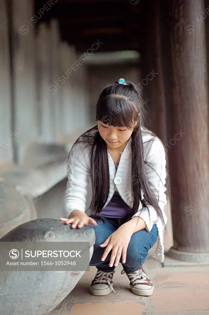 A young girl pats the head of a Turtle Stele statue at The Temple of Literature