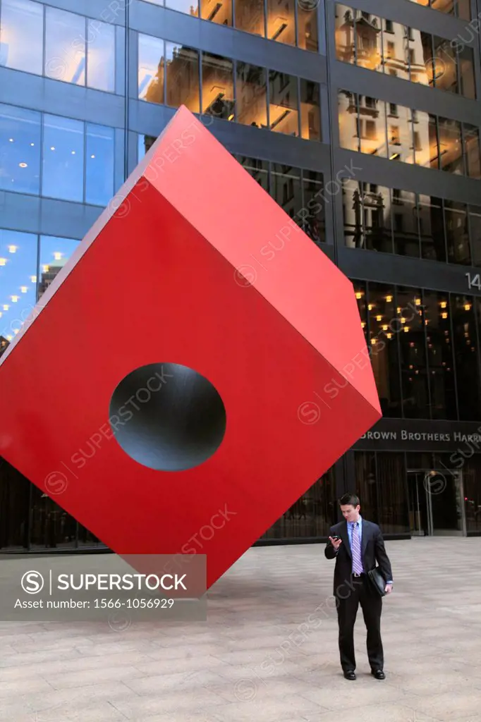 Man looking at his cellphone in front of the Red Cube a steel sculpture by Isamu Noguchi in plaza of HSBC building  New York City  New York  USANew Yo...
