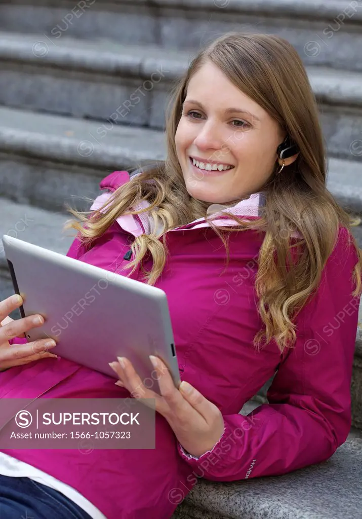 Beautiful young Caucasian woman taking with a bluetooth headset while holding a digital tablet