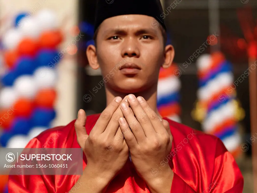 A traditionally dressed man in red holding his hands in prayer in Johor, Malaysia