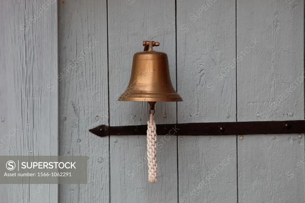 A small ship´s bell hanging on a white wooden door
