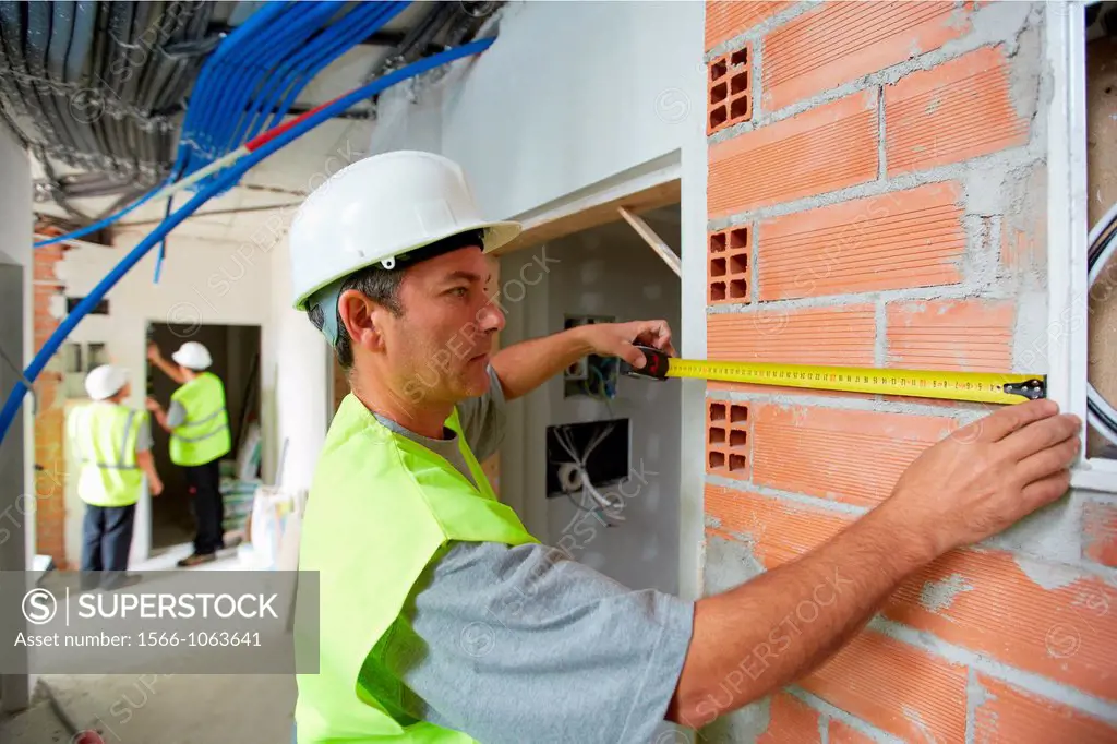 Worker with protective equipment, PPE, Taking retractable tape measures, housing construction, brick wall, Basque Country, Spain