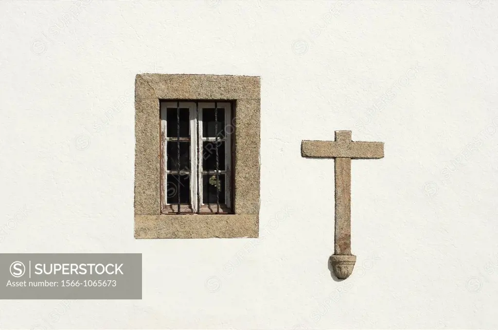 A window in an wall of an old Alentejo church with a stone cross on the wall