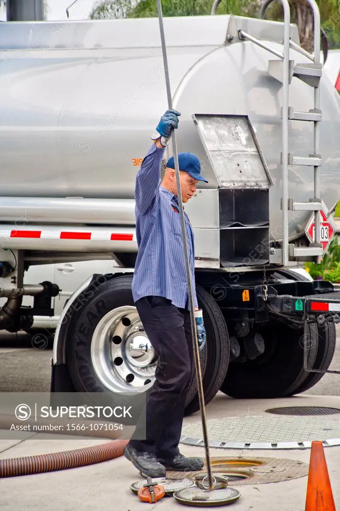 Using a long dip stick, a gasoline delivery man measures the levels in a service station´s underground storage tanks before adding additional fuel fro...