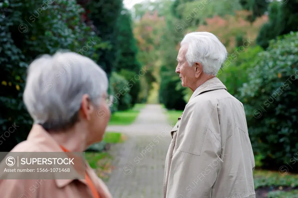 Senior caucasian woman with glasses looking at senior man, seen from backside, blurred green background, Hamburg, Germany, Europe