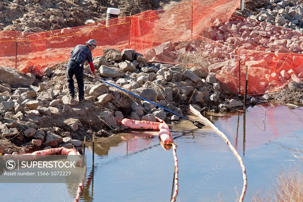 Commerce City, Colorado - A cleanup worker removes a tar-like substance from behind containment booms on Sand Creek near the South Platte River at the...
