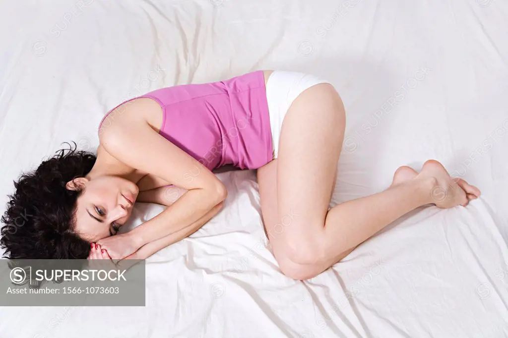 Young sad brunette woman lying down in bed