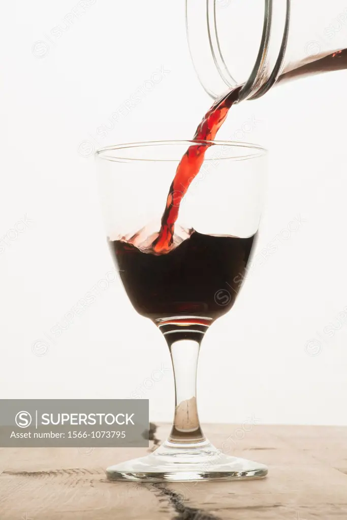 A glass of red wine being filled from a carafe
