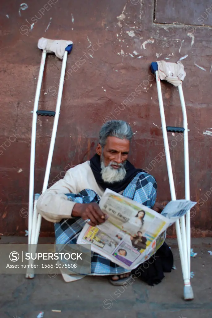 A muslim man with crutches is reading the newspaper in a street at Bombay, India.