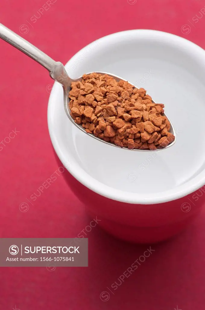 Spoon with instant coffee and cup filled with hot water