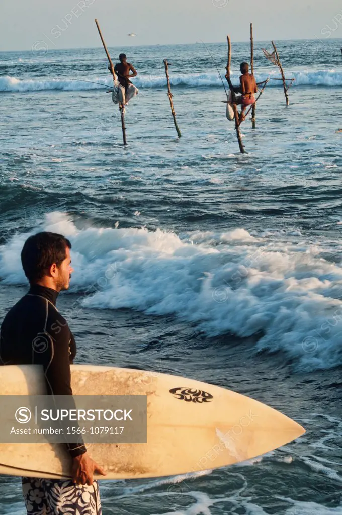 a surfer and stilt fishermen in Midigama, Sri Lanka