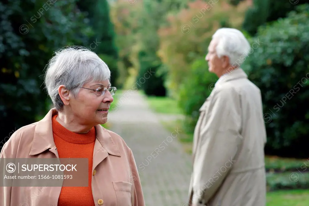 Senior caucasian woman with glasses, looking to the side with senior man seen from backside, blurred green background, Hamburg, Germany, Europe