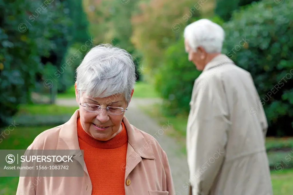 Senior caucasian woman with glasses, looking down with senior man in the background, blurred green background, Hamburg, Germany, Europe