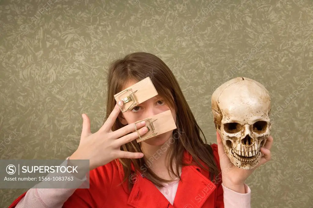 Preteen girl, with mousetraps on her fingers, holding a skull