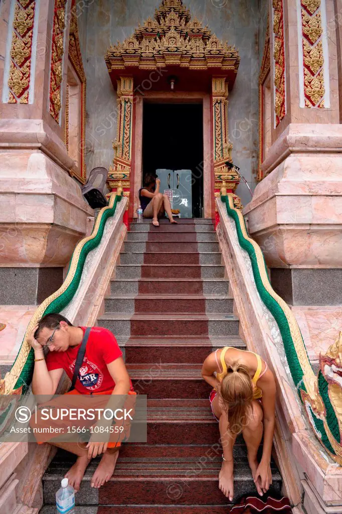 Tired European tourists resting at entrance to Wat Chalong - Buddhist temple in Phuket, Thailand  Wat Chalong is the largest and the most visited of P...