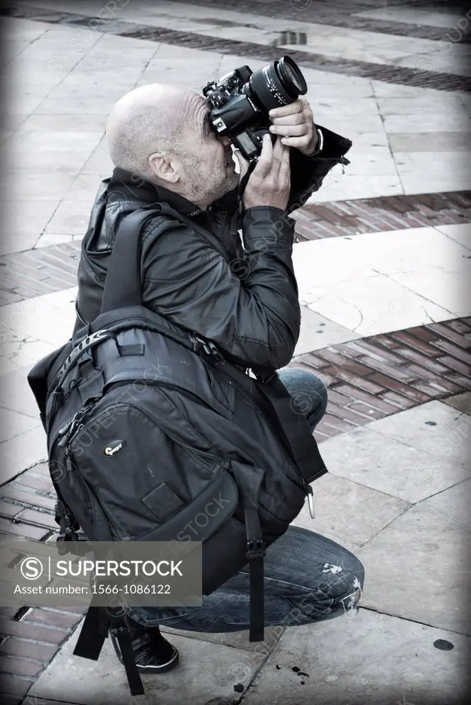 Professional Photographer backpacking, crouching and concentrate, taking photos with a digital SLR camera.