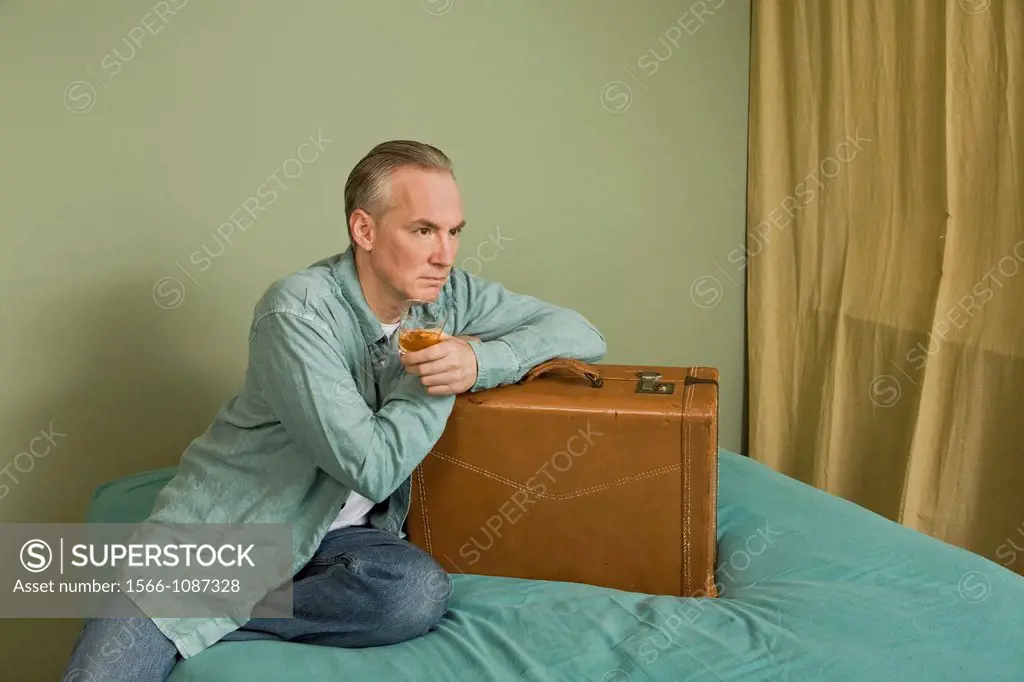 Middle-age man sitting on a bed with a suitcase