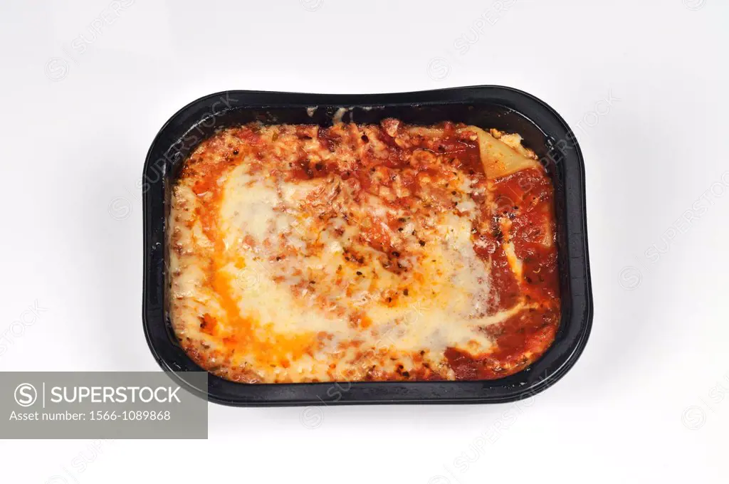 Cooked lasagna readymeal in black plastic tray on white background cutout