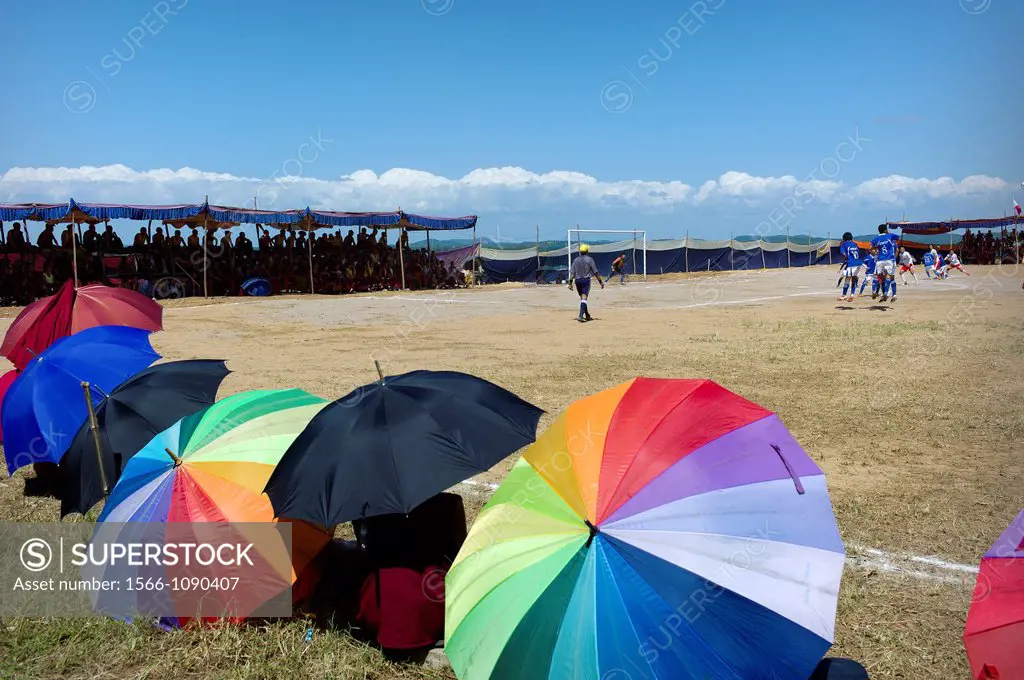 Buddhist monks sitting on the floor with colored umbrellas on a football field Mungod, India