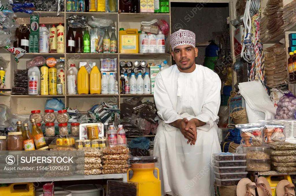 An Arab merchant sitting among his merchandise at a market stall on the bazar of Nizwa, Sultanate of Oman
