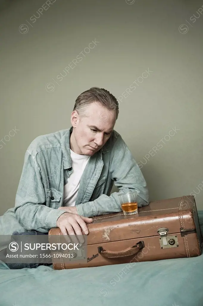 Middle-age man with a drink setting on a suitcase