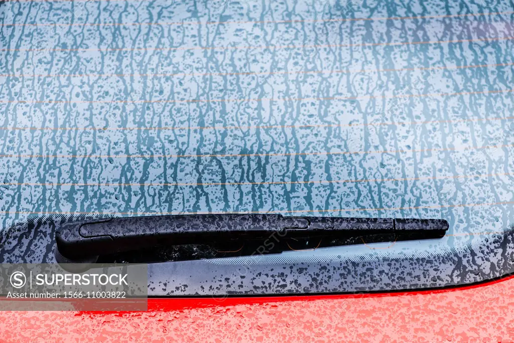 Detail of wet red car. Windshield wiper and a rainy window.