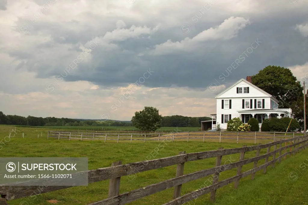 Gathering storm clouds on a farm with a wood fence, white farm house and pasture in summer