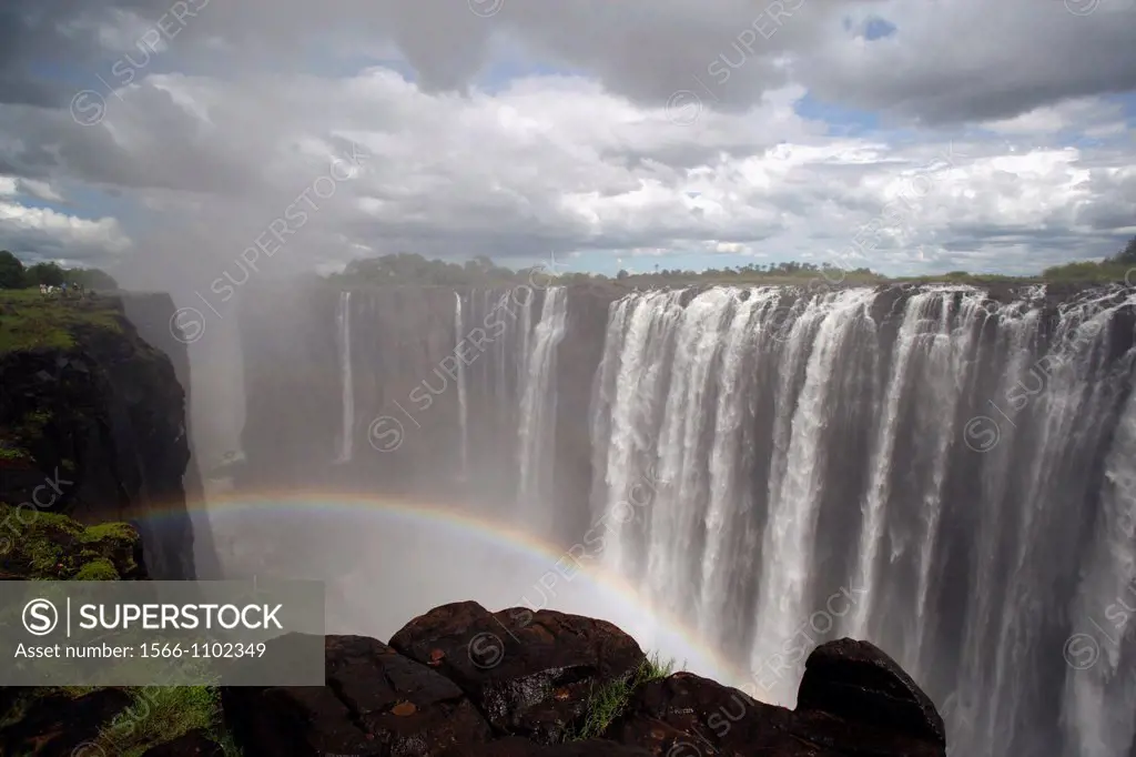 Victoria Falls with rainy clouds, view into the canyon of the Zambezi river, people seen on the left edge of the rocks, Zimbabwe