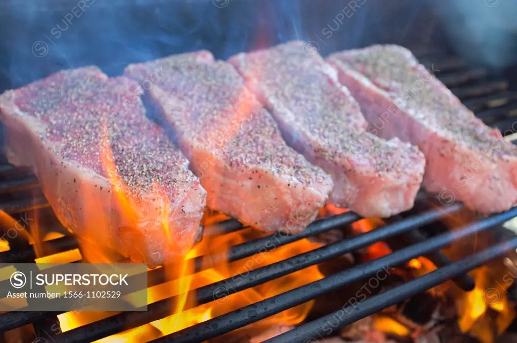 Seasoned beef strip loin steaks grilled over hot fire barbecue pit