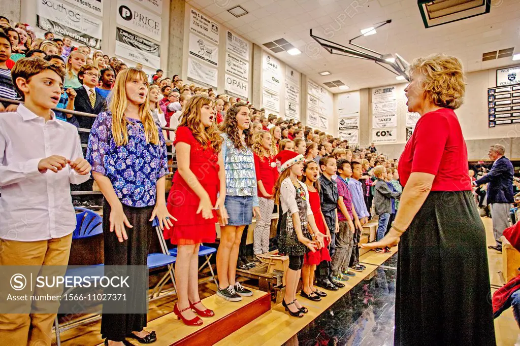 A music teacher directs multiracial middle school children singing Christmas carols as a group at a school concert in Aliso Viejo, CA.