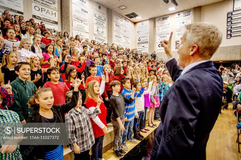 A music teacher directs multiracial middle school children singing Christmas carols as a group at a school concert in Aliso Viejo, CA.