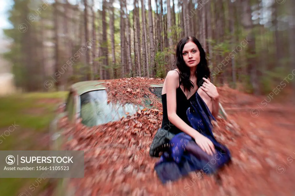 Portrait of a 20 year old brunettte woman sitting on an old car in a forest setting