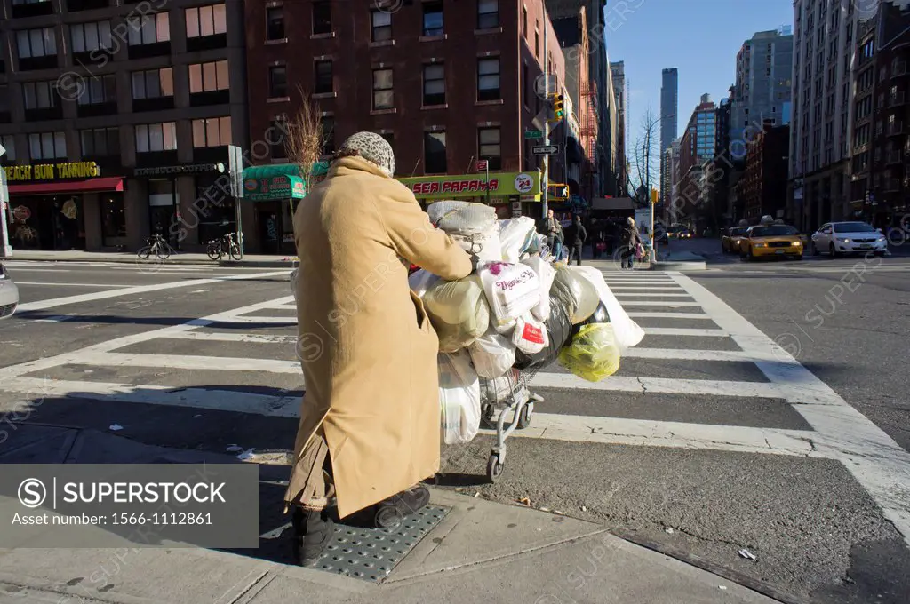 Woman with her possessions on a shopping cart crosses Seventh Avenue in the Chelsea neighborhood of New York