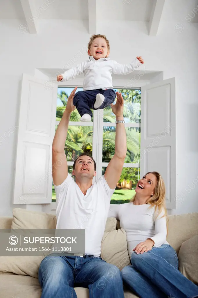 Family on their sofa throwing one year old baby in the air