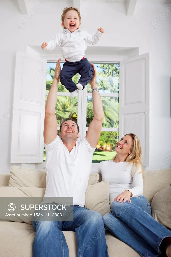 Family on their sofa throwing one year old baby in the air