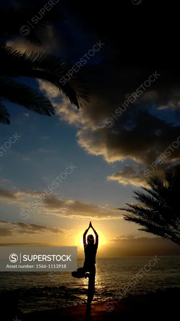 A young women practises the art of Yoga over a beautiful sunset at Tenerife beach