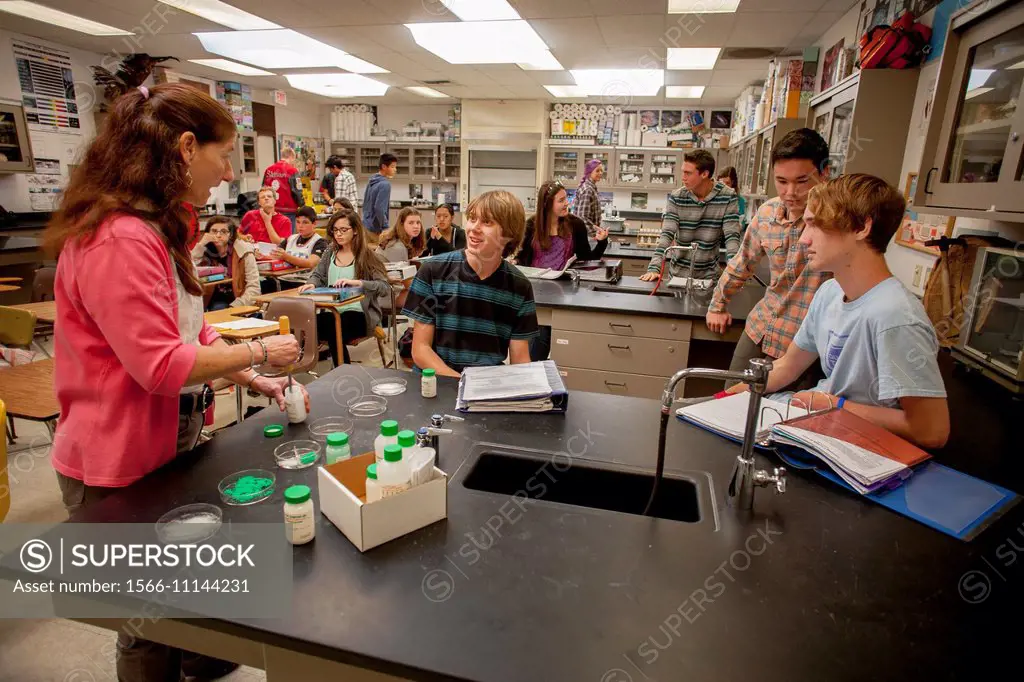 A high school chemistry teacher talks with multiethnic students while she prepares a classroom experiment in San Clemente, CA.
