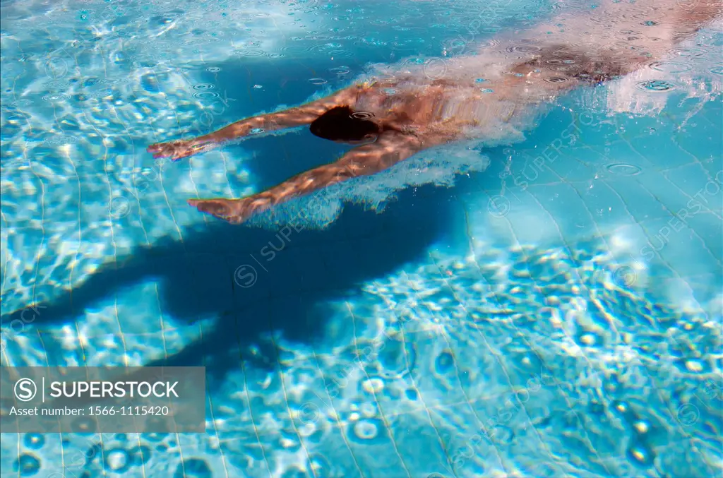young man swimming under water in the swimming pool in companionship of his shadow