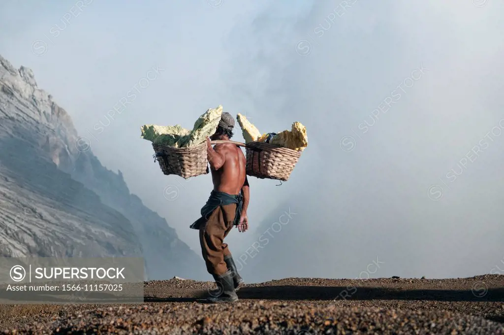 Miner carrying a heavy load of sulphur at the Kawah Ijen volcanic crater, Java, Indonesia.