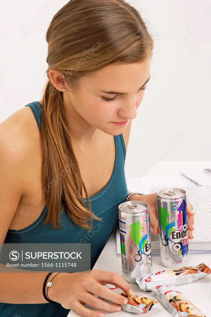 Teenage girl doing her homework and using her computer, while eating sweets, cookies, and drinking energy drinks